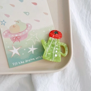 Green marble pattern teapot brooch with red tomato lid on a minimalist ceramic tray