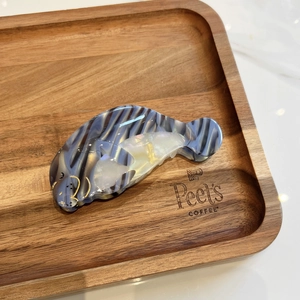 Dettaglio molletta per capelli in acetato a forma di lamantino con trama marmorizzata blu