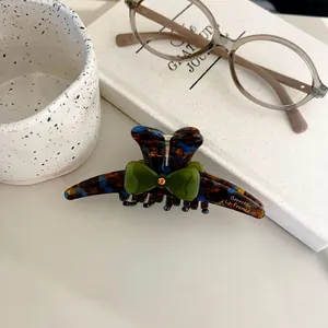 Elegant tortoiseshell hair claw with green bow and orange crystal detail in vintage style