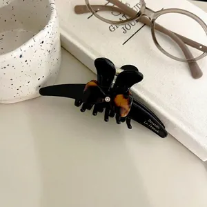 Detailed view of black acetate hair claw with a tortoiseshell bow and crystal accent