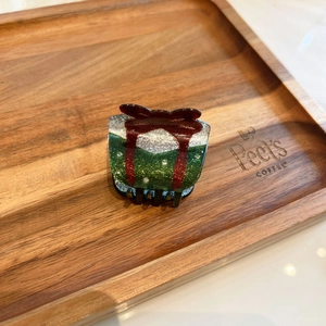 Dettaglio della molletta per capelli a forma di pacco regalo verde con fiocco rosso