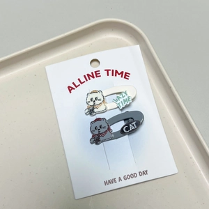 Detailed view of cat-shaped hair clips in cream and grey on display card