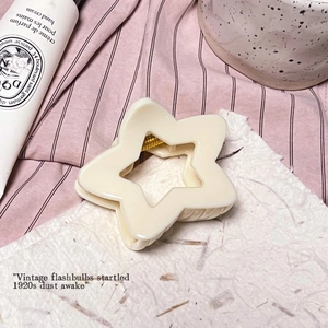Détail d'une pince à cheveux étoile crème avec ressort en métal doré sur une carte texturée