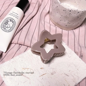 Détail d'une pince à cheveux étoile mate mauve avec ressort doré sur papier texturé