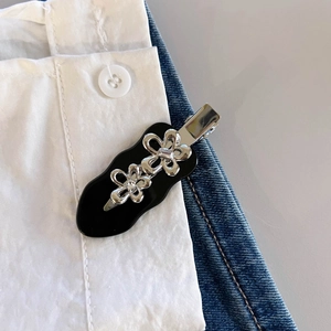 Dettaglio di una molletta in acetato nero con fiori di metallo su denim blu
