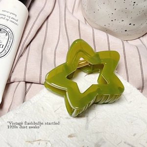 Détail d'une pince à cheveux étoile vert olive avec ressort doré posée sur papier blanc