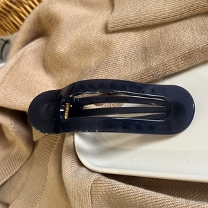 Close-up of a dark blue oval hair claw clip with golden metal spring on a white ceramic plate