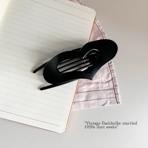 Close-up of matte black heart-shaped hair claw clip with cutout design on notebook