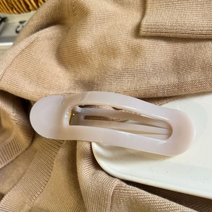 Detail of cream oval hair claw clip with glossy finish on a soft knitted sweater