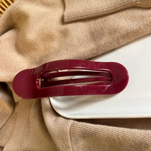 Detail of burgundy glossy hair claw clip on beige knitwear with internal metal spring