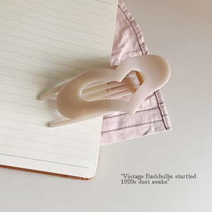 Detail of a cream-colored hollow heart hair claw clip with golden metal spring