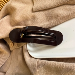 Detail view of a chocolate brown hair claw clip with glossy finish and gold metal spring