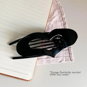 Close-up of a glossy black heart-shaped hair claw clip on a minimalist aesthetic background