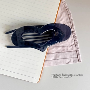Detail of dark translucent heart hair claw clip on a notebook and striped fabric background