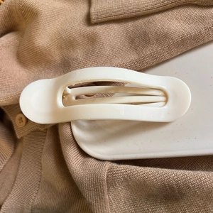 Minimalist white oval hair claw clip detail on beige knitwear and white tray