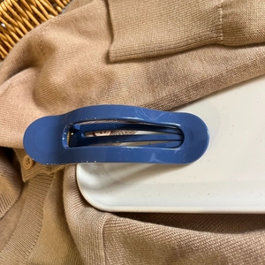 Detail of glossy blue oval hair claw clip resting on a white ceramic plate