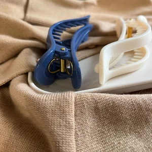 Detail of blue and beige matte wavy hair claws on a ceramic tray over cozy knitwear
