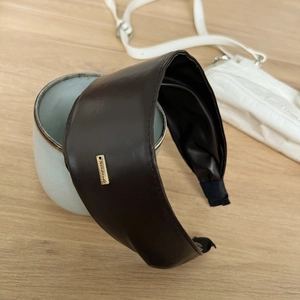 Detail view of wide dark brown faux leather headband with handmade golden metal tag