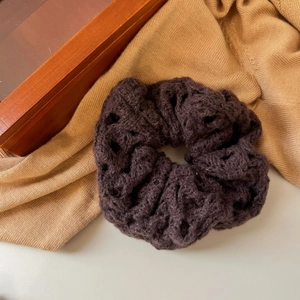 Detail shot of a dark brown hollow knit scrunchie on a warm autumn texture background