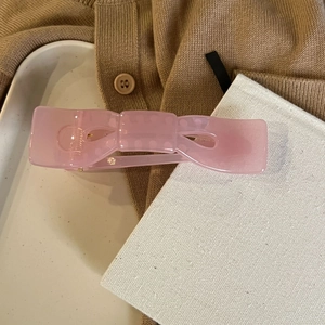Detailansicht einer rosa Haarspange aus Harz in Schleifenform auf Strickstoff