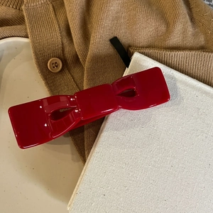 Detailansicht einer glänzenden roten Schleife-Haarklammer auf einem Strickpullover