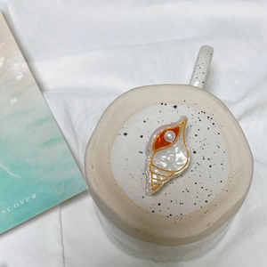 Détail de la pince à cheveux coquillage avec bords dorés, perle blanche et émail orange