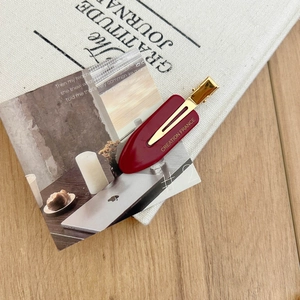 Elegant dark red acetate hair clip with gold logo on a minimalist canvas background