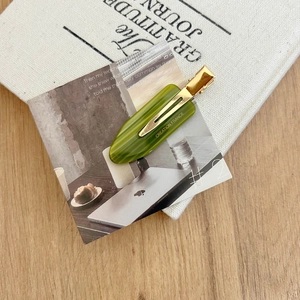Detail of French acetate hair clip in olive green with gold logo on aesthetic background