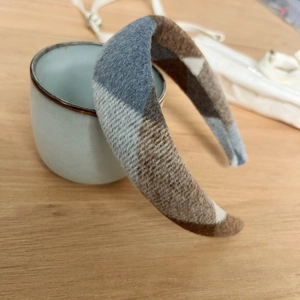 Detail of a thick plaid wool headband with blue and brown check pattern on a ceramic cup