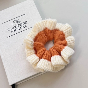 Détail d'un chouchou en maille orange et beige avec texture ondulée posé sur un livre