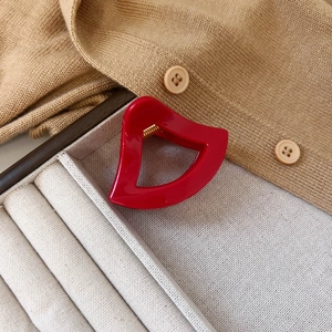 Detailansicht der roten Lippen-Haarklammer auf beigem Pullover mit Goldfeder