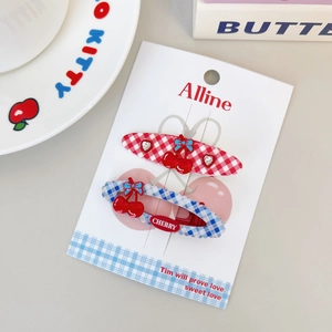 Detail of red and blue checkered hair clips with cherry charms on a branded display card