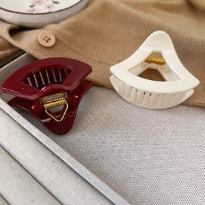 Nahaufnahme geometrischer hohler Haarklammern in Burgund und Creme mit Goldfeder