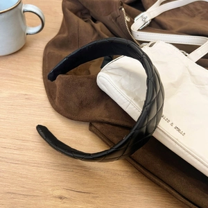 Dettaglio cerchietto in pelle nera trapuntata con motivo a rombi per un elegante stile retrò