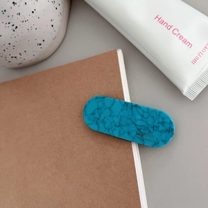 Close-up of blue marble pattern hair clip with gold logo on a cozy desk setup
