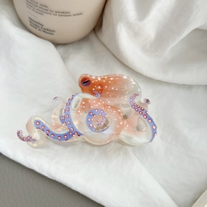 Cute octopus hair claw clip with orange marble pattern and purple tentacles on fabric