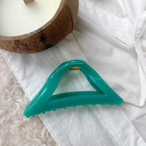 Detailed macro shot of a clear cyan hollow triangular hair claw clip on soft white fabric