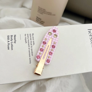 Nahaufnahme der rosa-weiß karierten Haarspange mit Strasssteinen und goldenem Clip