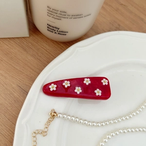 Fermaglio per capelli floreale in resina rossa con fiori bianchi su un piatto di ceramica