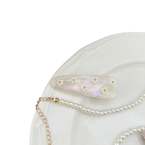 Fermaglio per capelli a fiori iridati e collana di perle in un piatto di porcellana