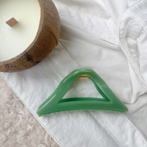 Detail view of a green triangular hair claw clip on white lace and rug background