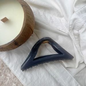 Deep gray hollow triangle hair claw clip resting on a white lace fabric background