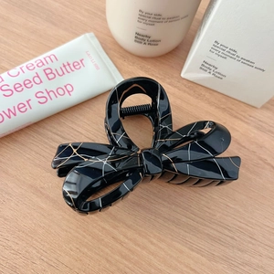 Elegant French black ribbon hair claw clip with golden marble patterns on wooden desk