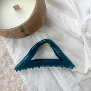 Deep teal triangular hair claw clip with golden spring on elegant lace background