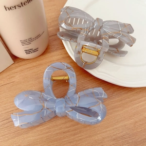 Detail of elegant resin hair claws with gold thread marble texture and bow design