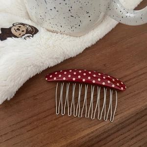 Close-up of red polka dot hair comb with silver metal teeth on a wooden surface