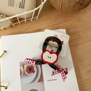 Detalle de pinza para pelo de carey con diseño de manzana y lazo rojo en tarjeta