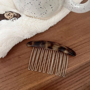 Close-up of handmade tortoiseshell acetate hair comb with golden logo and metal teeth