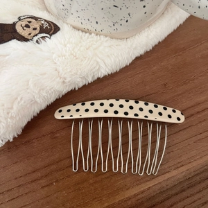 Polka dot oval acetate hair side comb with silver metal teeth on a wooden surface