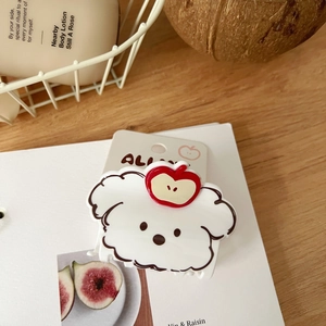 Detalle de una pinza para el cabello de cachorro blanco con manzana roja decorativa